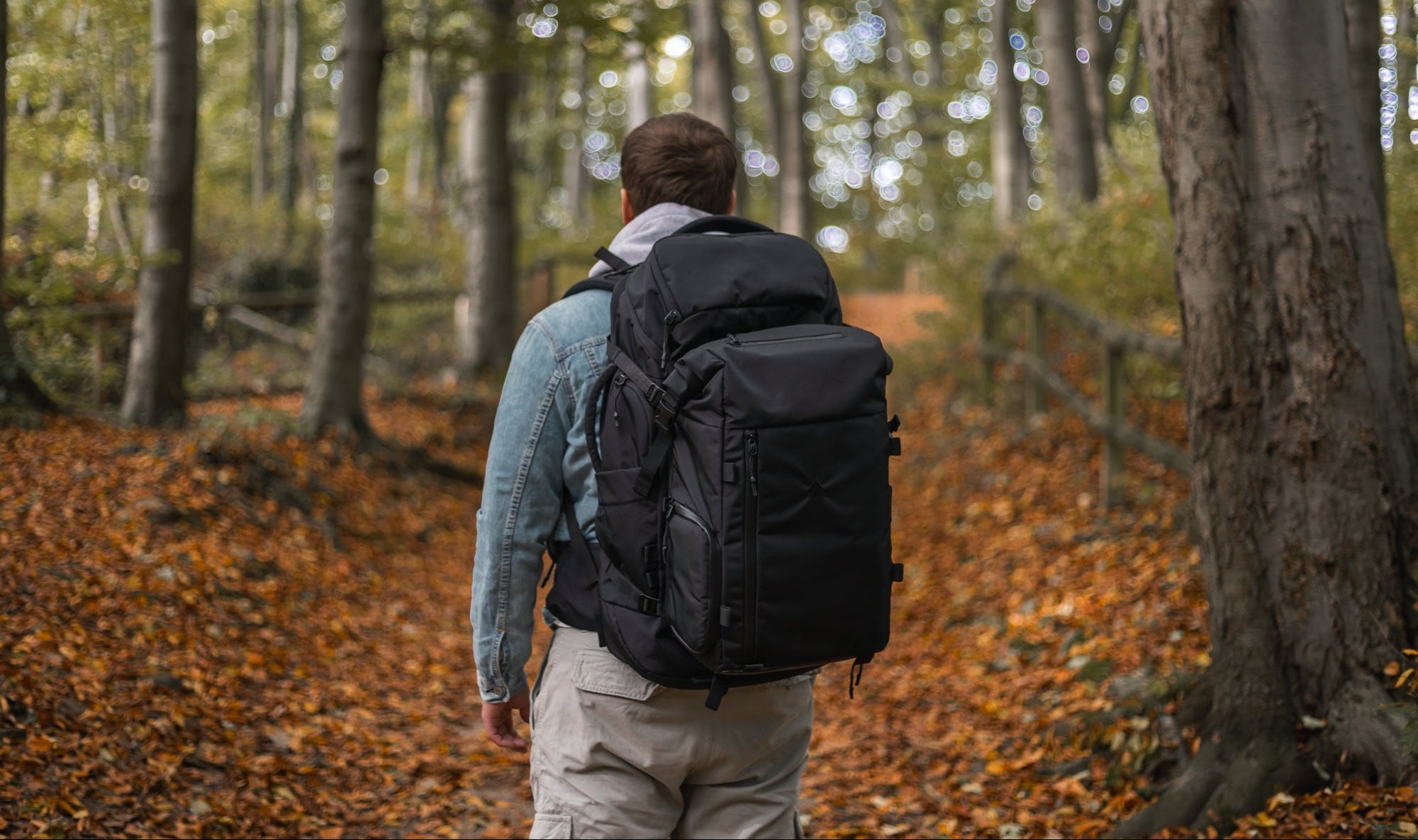 Person with a black backpack walking through a forest with autumn leaves