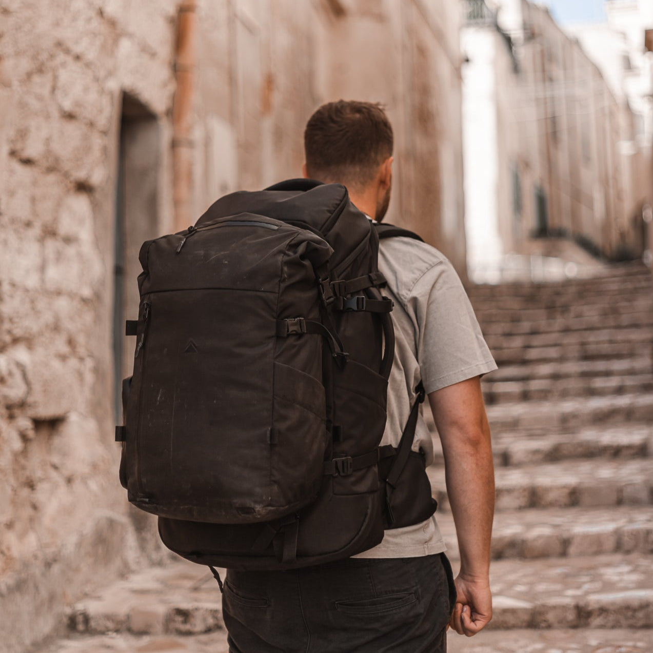 Man with a black backpack walking down a stone alleyway.